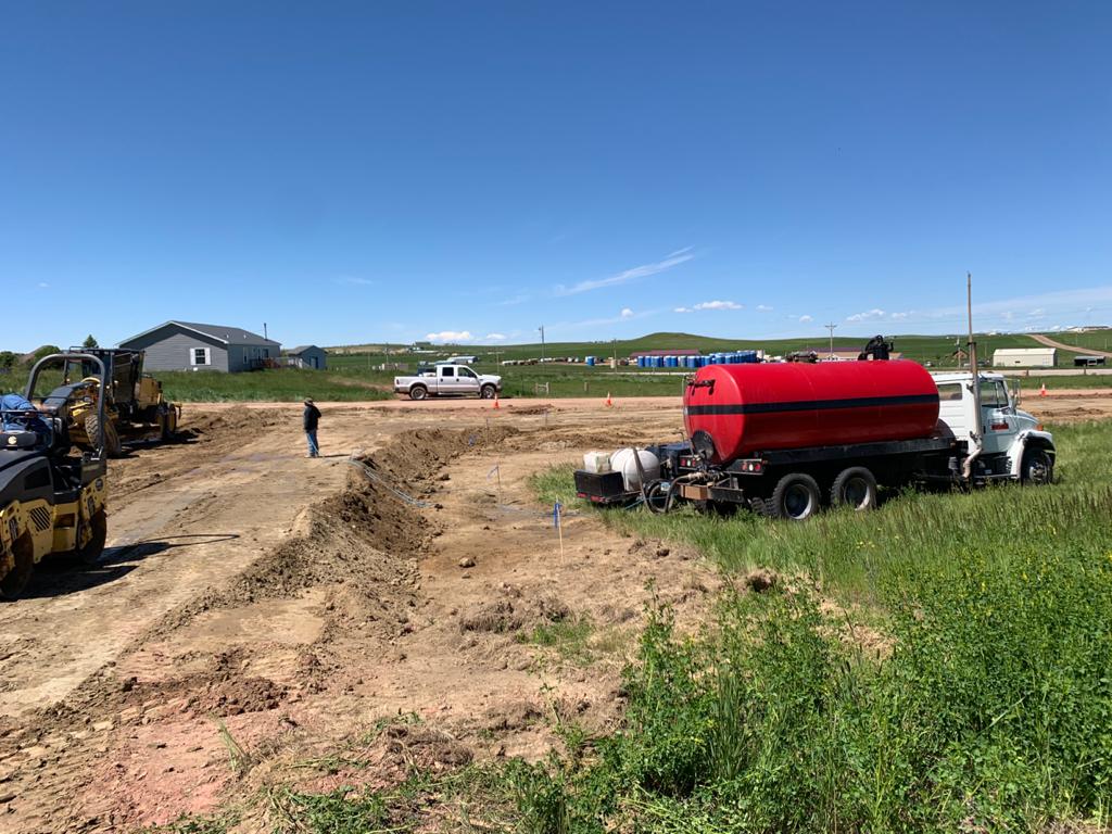 A red truck parked in the dirt near some buildings.