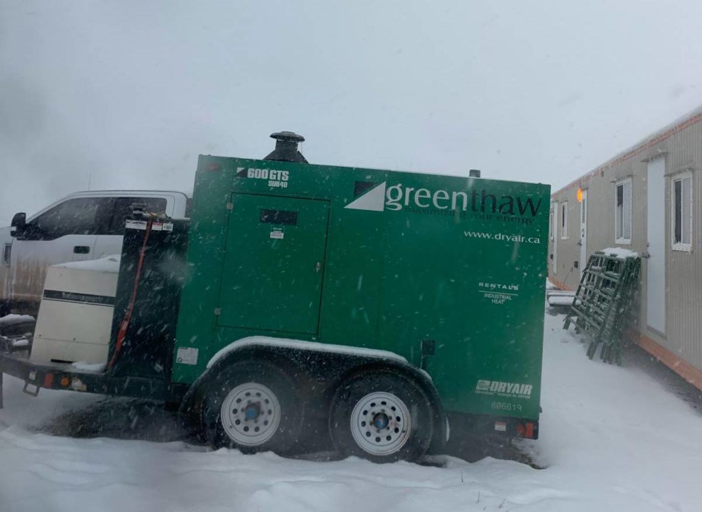 A green snow plow truck is parked in the snow.