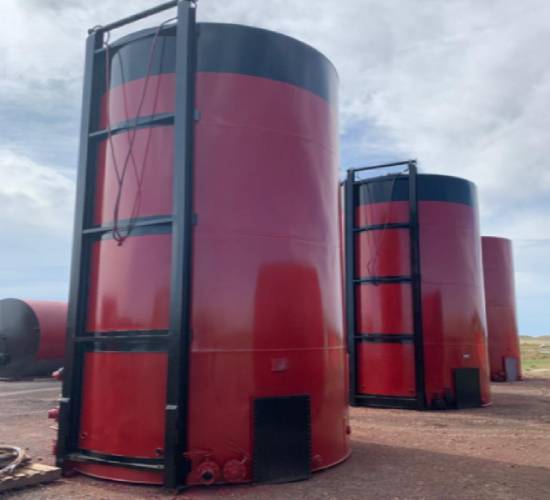 A group of large red tanks sitting on top of a dirt field.